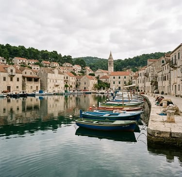 Colorful fishing boats moored in calm Milna harbor with stone buildings on Brač island