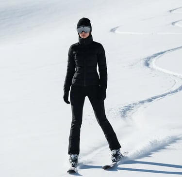 A woman skiing on a sunlit slope wearing a form-fitting black thermal ski suit, a black beanie, and 
