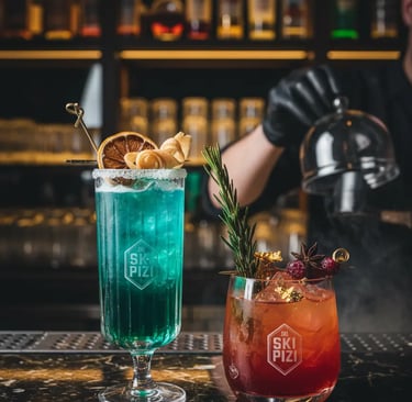 wo vibrant après-ski cocktails, one turquoise and one red, served on a dark marble bar at Ski Pizi w