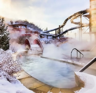 Steaming outdoor thermal pool with a wooden bridge and a large water slide in the background during 