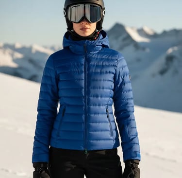 Front view of a woman wearing a stylish sapphire blue ski jacket paired with black ski pants and a h