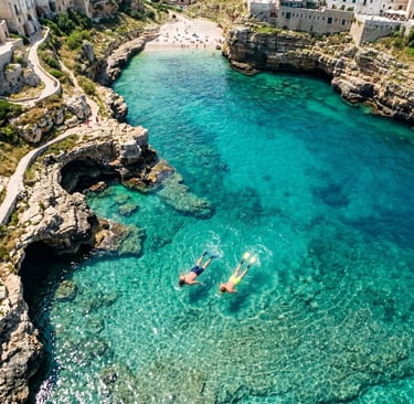 Overhead drone view of two snorkelers in turquoise water near Polignano a Mare rocky coast