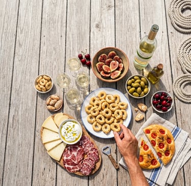 Overhead view of taralli, burrata, figs, salumi and white wine on wooden boat deck