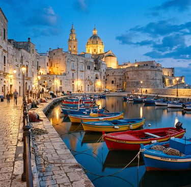 Colorful fishing boats in Monopoli Porto Vecchio harbor with cathedral dome at blue hour, Puglia