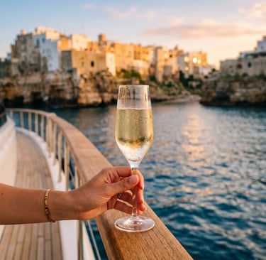 Hand holding chilled Apulian prosecco glass on yacht deck, Polignano a Mare cliffs at golden hour