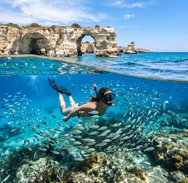 Snorkeler exploring fish school underwater near Sant'Andrea limestone arch on Salento coast, Italy