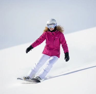 Woman in a pink ski jacket skiing down a slope on a sunny day in Grindelwald.