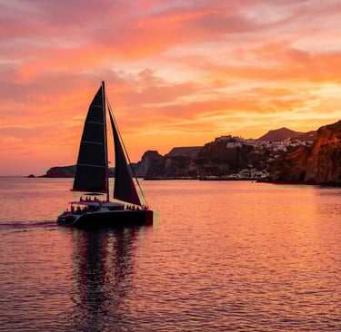 Premium catamaran sailing back to Milos harbor under vibrant orange sunset sky