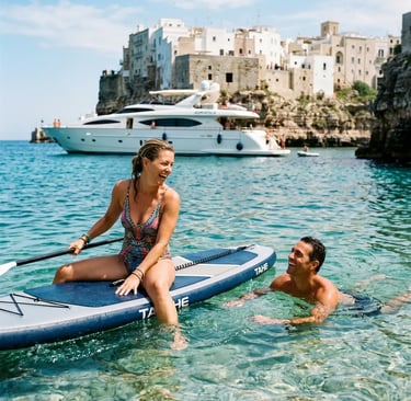 Smiling couple on SUP paddleboard next to luxury yacht in turquoise water of Polignano a Mare