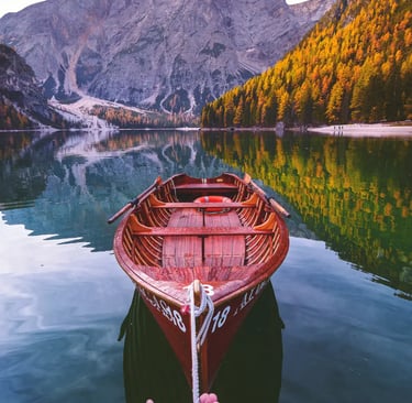 Hand holding rope of wooden rowboat on Lake Braies with autumn Dolomite reflections