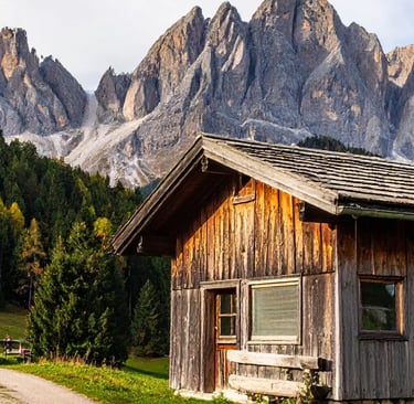 Rustic alpine cabin glowing in golden light with dramatic Dolomite peaks behind