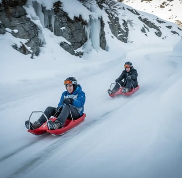 Two people in winter gear sliding down a snowy hill on red plastic sleds during a winter vacation.