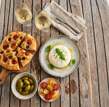 Overhead view of burrata, focaccia, olives, tomatoes and white wine on teak boat deck