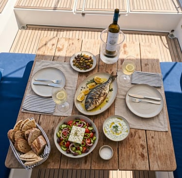 Fresh Greek lunch with grilled fish, salad, olives and white wine served on catamaran deck.