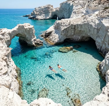 Two swimmers in crystal-clear turquoise water between white rock arches at Kleftiko, Milos, Greece