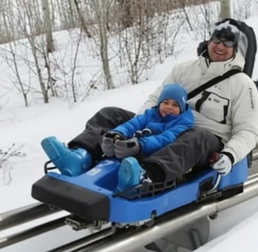 Close-up of a young boy in a blue jacket and beanie enjoying a mountain coaster ride on a snowy trac