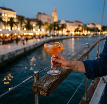 Hand holding cocktail on sailboat railing with Split Riva promenade lights at dusk