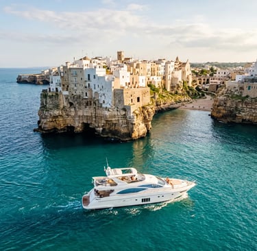 White luxury yacht sailing past Polignano a Mare cliffs and old town on turquoise Adriatic sea