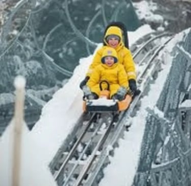 An adult and child in bright yellow winter gear riding a mountain coaster together through a snowy, 