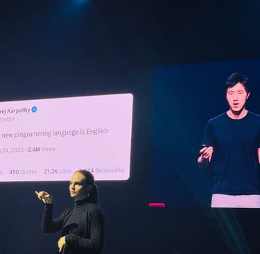 an ASL interpreter at a tech conference in front of a screen that shows a speaker next to a tweet