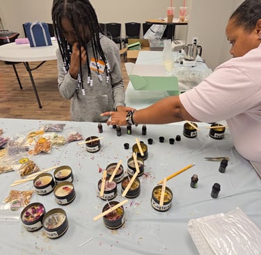 A child and adult instructor work together at a DIY candle making workshop with tins and essential oils.
