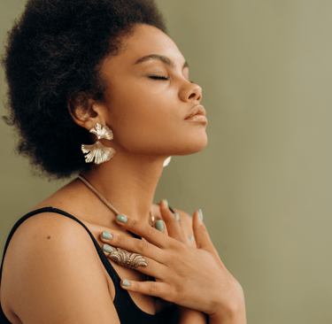 Black woman with afro hair wearing gold statement earrings and a ringset with green manicure.