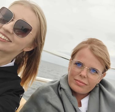 Dwie kobiety na katamaranie. Jedna w okularach przeciwsłonecznych i czarnej bluzie.
