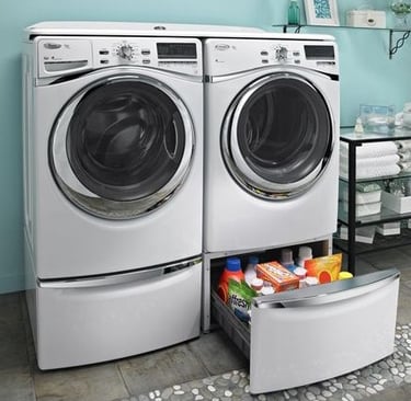 Front-loading washer and dryer in a laundry room with a storage drawer containing detergent and cleaning supplies underneath.