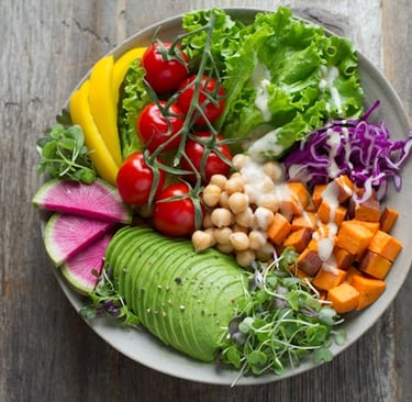 A vibrant vegan Buddha bowl with sliced avocado, sweet potato, chickpeas, and fresh vegetables on a wooden table.