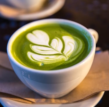 A white cup of green matcha tea latte with a leaf-shaped foam art design