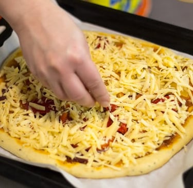 Hand sprinkling shredded cheese on a homemade pizza with tomatoes on a baking sheet.