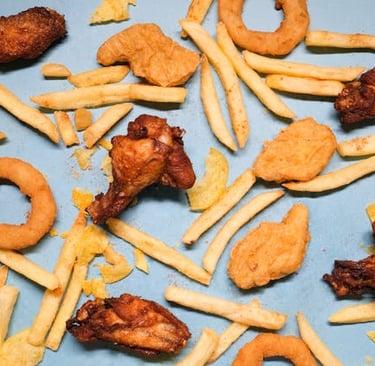 Flat lay of crispy fried chicken wings, chicken nuggets, french fries, and onion rings on a blue background.