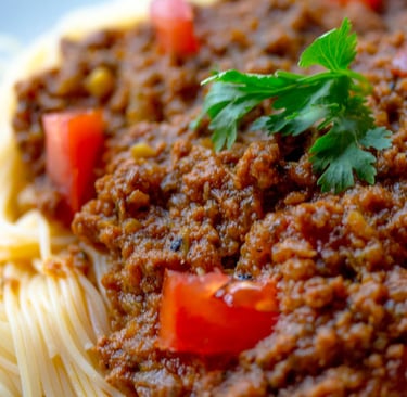 A close-up of spaghetti bolognese topped with fresh diced tomatoes and a sprig of parsley.
