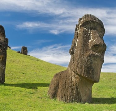 Ancient Moai stone statues on a grassy hill at Easter Island under a blue sky.