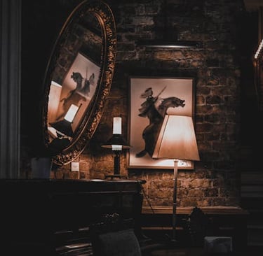 Vintage living room with warm lamp lighting, a large round mirror, and framed art against a rustic brick wall.