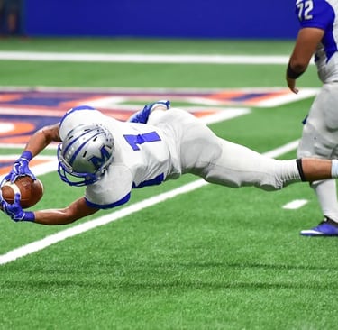 Football wide receiver making a spectacular diving catch on green turf during a game.