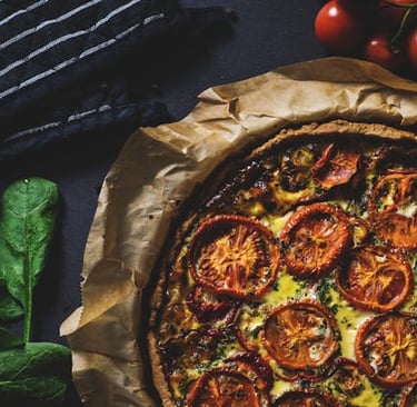 Homemade tomato and spinach quiche on baking paper with fresh ingredients on a dark surface.