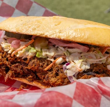 Pulled beef sandwich topped with creamy coleslaw on a toasted bun in a red checkered basket.