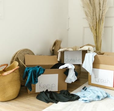 Clothing decluttering and home organization using cardboard boxes labeled keep, donate, and trash.