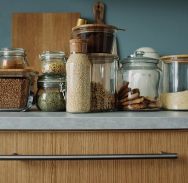 A collection of glass jars with wooden lids containing grains and snacks for organized kitchen storage.
