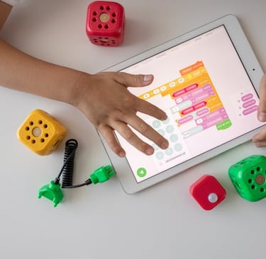 A child uses a tablet for visual coding with colorful STEM blocks and educational toys.