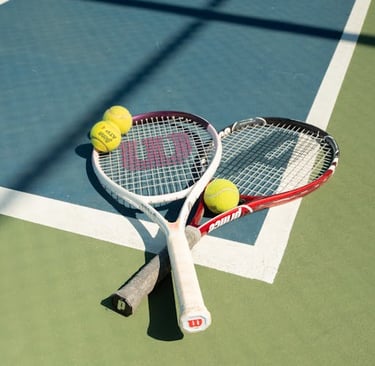 Two tennis rackets and yellow tennis balls on a blue and green outdoor hard court.