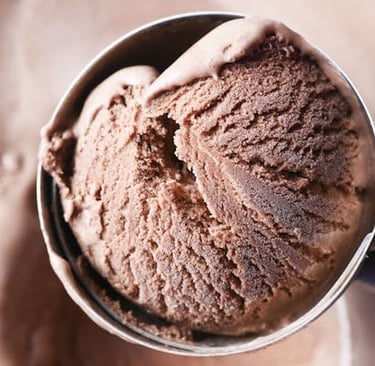 A metal scoop picking up a textured scoop of creamy gourmet chocolate ice cream.