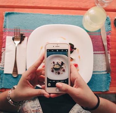 a person holding a cell phone in front of a plate, thinking of tips to write compelling captions