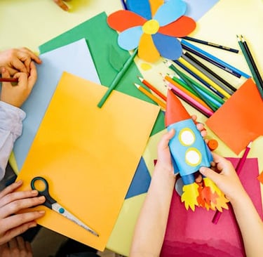 Child crafting a paper rocket at a table with colorful construction paper, scissors, and pencils.