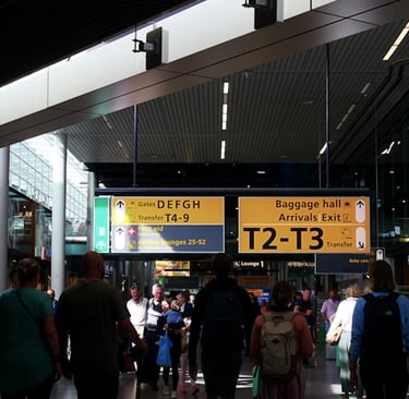 Crowd of travelers walking through a busy airport terminal past directional signs for gates and baggage.