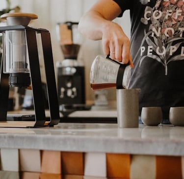 Barista pouring specialty drip coffee from a glass carafe into a ceramic mug, coffee brewing methods