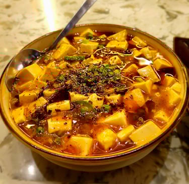 Bowl of Mapo tofu sprinkled with crushed Szechuan peppercorns with floating peas