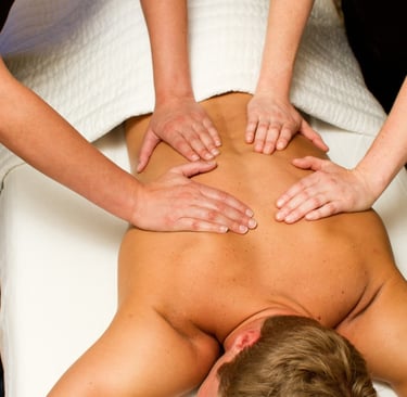 Masaje a cuatro manos realizado por dos terapeutas profesionales sobre la espalda de un hombre