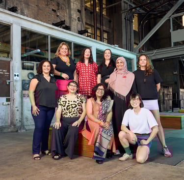 A group of nine people standing, sitting and kneeling in a cavernous industrial space.